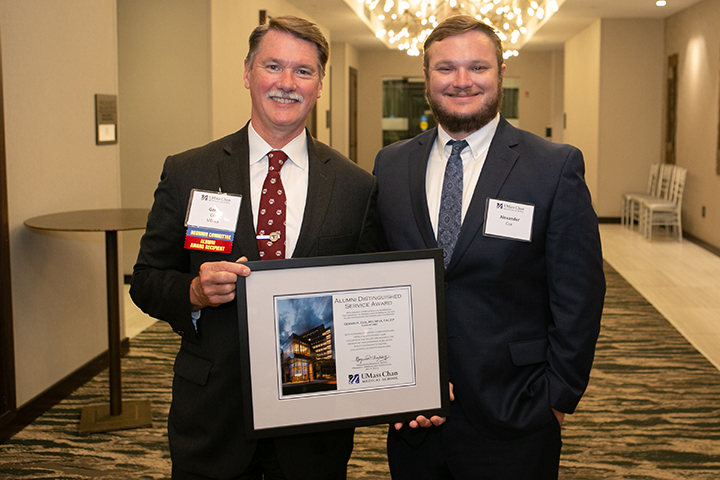 Gerry Cox, holding his Distinguished Alumni Award, alongside his son, Alex Cox.