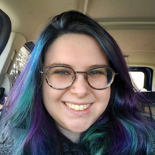 white woman with blue and purple long hair wearing glasses