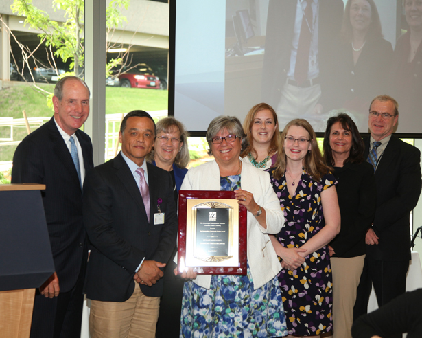 President and CEO Toni Maguire, RN, MPH, holds the award she accepted on behalf of the Edward M. Kennedy Community Health Center, flanked by staffers and Chancellor Collins and Dean Terence Flotte.