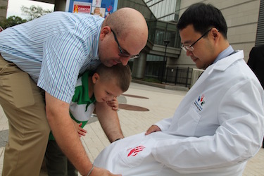 Kenneth Laferriere helps his son, Kaiden, put a red handprint on the pocket of the new Hyundai Hope on Wheels lab coat given to grant awardee Wen Xue, PhD.