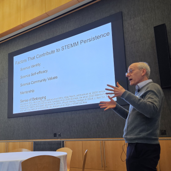 Man presenting with a slide about STEMM workforce persistence in the background