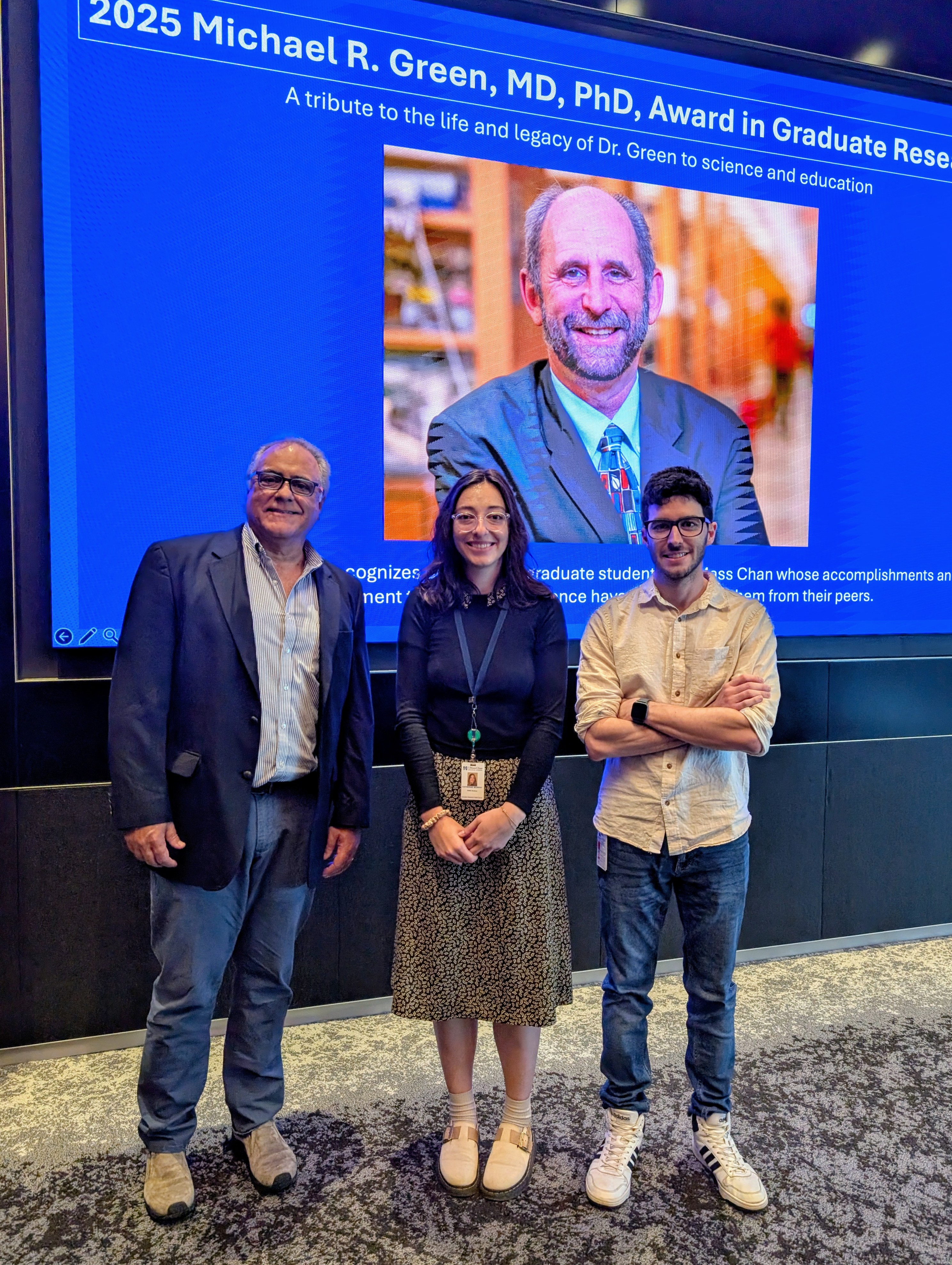 Lucio Castilla, Katherine Murphy and Ezequiel Calvo-Roitberg standing in the auditorium in front of a screen showing a photo of Michael Green