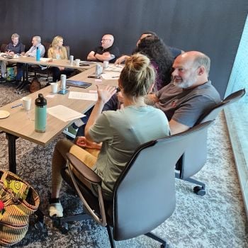 Eight people seated around conference room tables, talking to one another in pairs