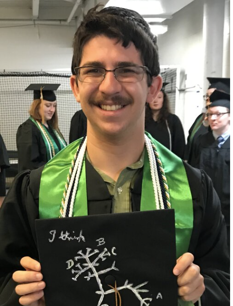 a man smiles for the camera in graduation regalia