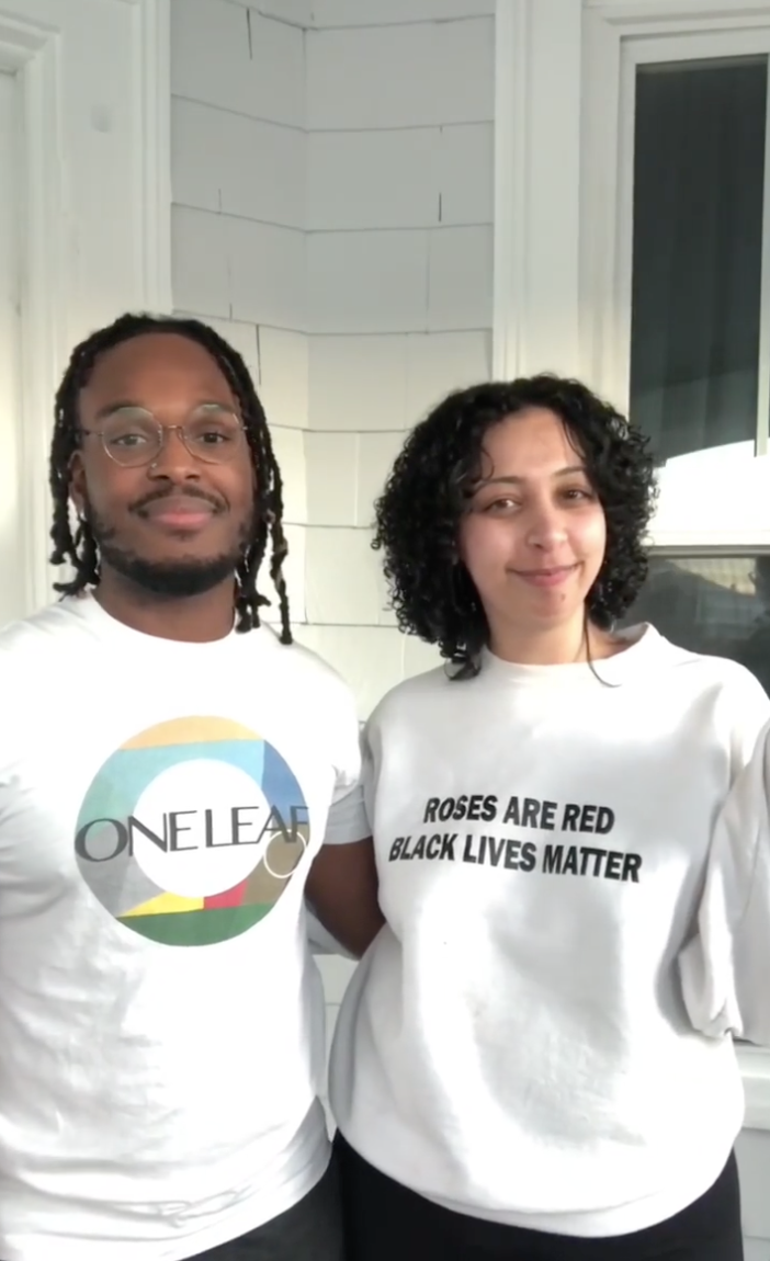 Two people standing together and smiling at the camera. One is wearing a One Leaf Corp tshirt and the other is wearing a shirt that says "roses are red, black lives matter."