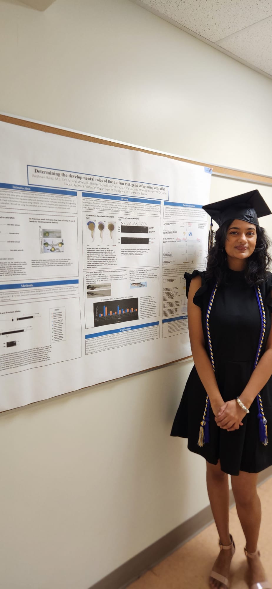 A woman standing next to a scientific presentation poster hung in a hallway