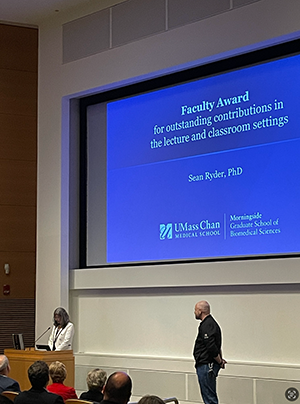 a picture of Dr. Sean Ryder standing at the front of a lecture hall to receive an award
