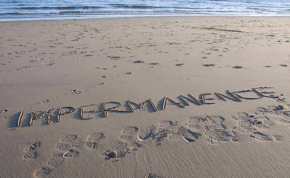 The word impermanence written on a sandy beach