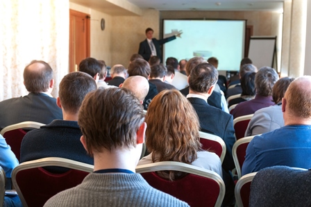 People watching a presentation by a man in a large room