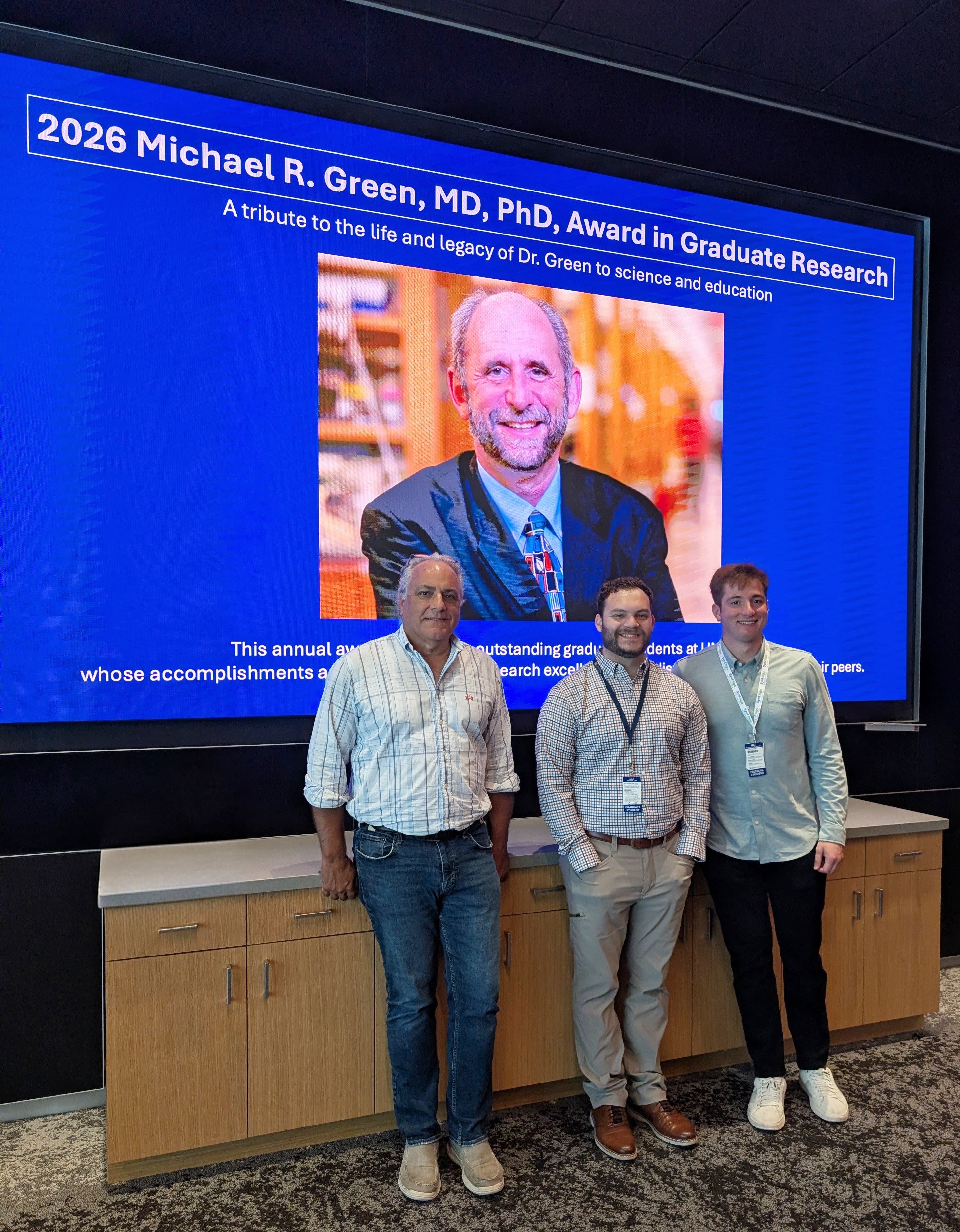 Lucio Castilla, Brennon Berard and Andrew Petti standing in the auditorium in front of a screen showing a photo of Michael Green.