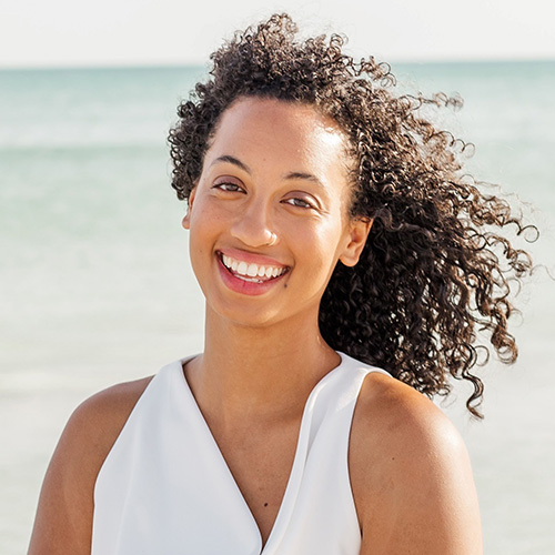 Black woman smiling wearing a white blouse standing on the beach