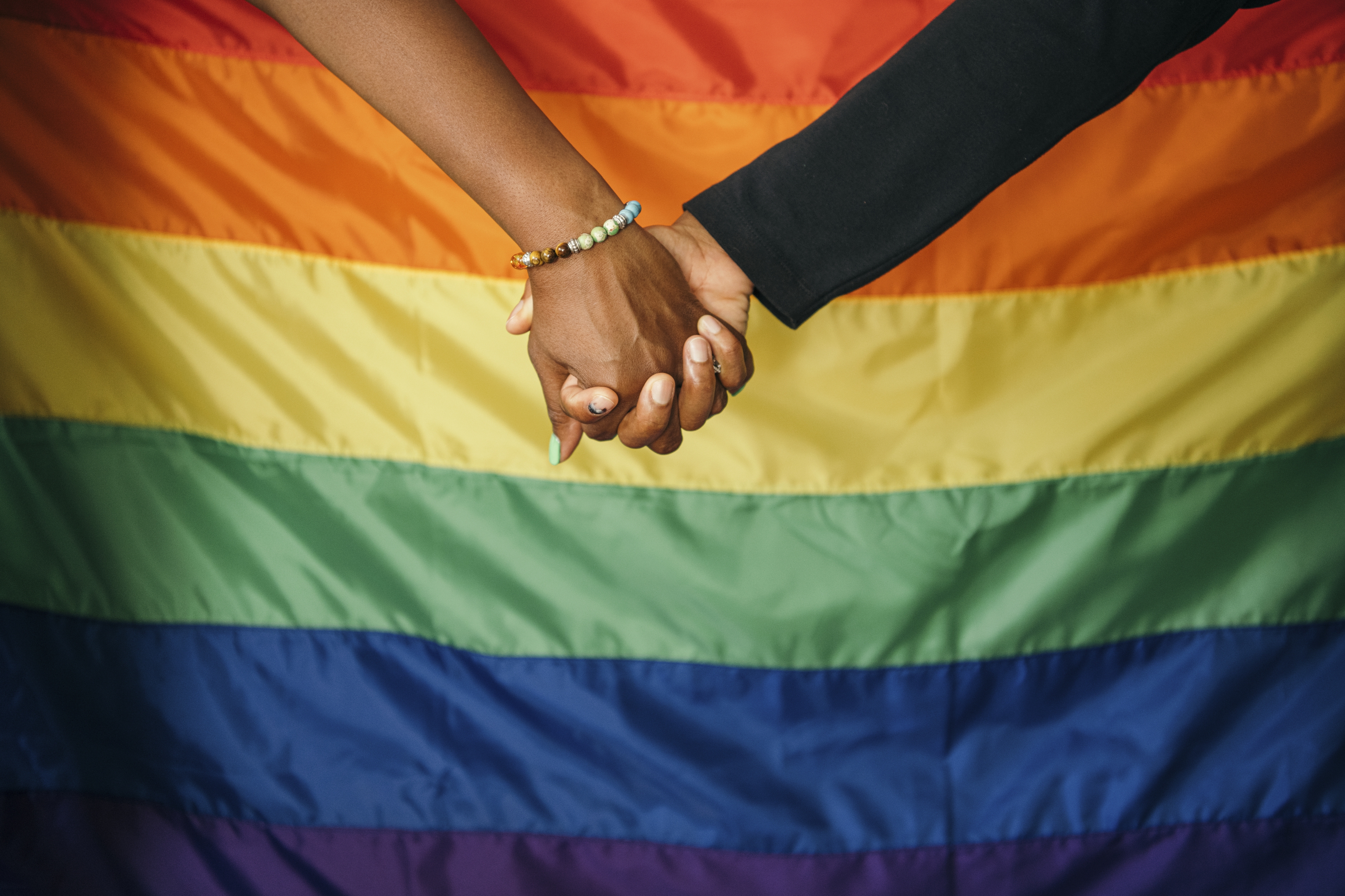 black hand and white hand holding hands in front of pride flag