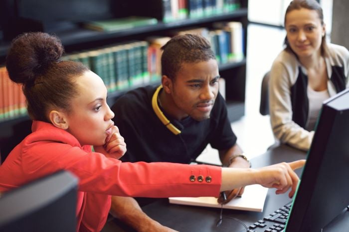 3 college students in a library on the computer