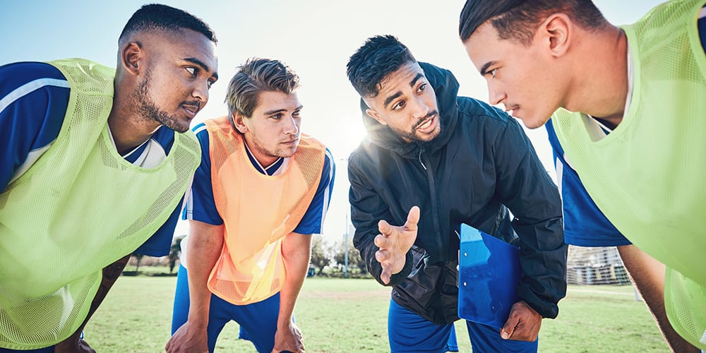 group of male teens talking to coach on a soccer field