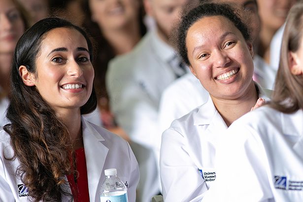 Mary Bassaly (left) and Bethany Berry are all smiles as classmates slip into their white coats on stage.