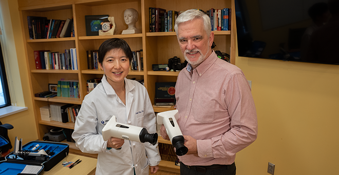 Juan Ding, OD, PhD, (left) and James Ledwith, MD, each holding an AI-assisted device being used in a pilot study to screen for diabetic retinopothy in a primary care setting. 