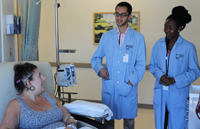 UMMS High School Health Careers participants (standing) Christian Barreto and Irene Yancey chat with patient Melissa Benoit during their internship in the UMass Memorial Medical Center oncology infusion clinic. 