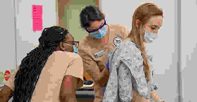 Nursing students perform a physical exam of a patient. 