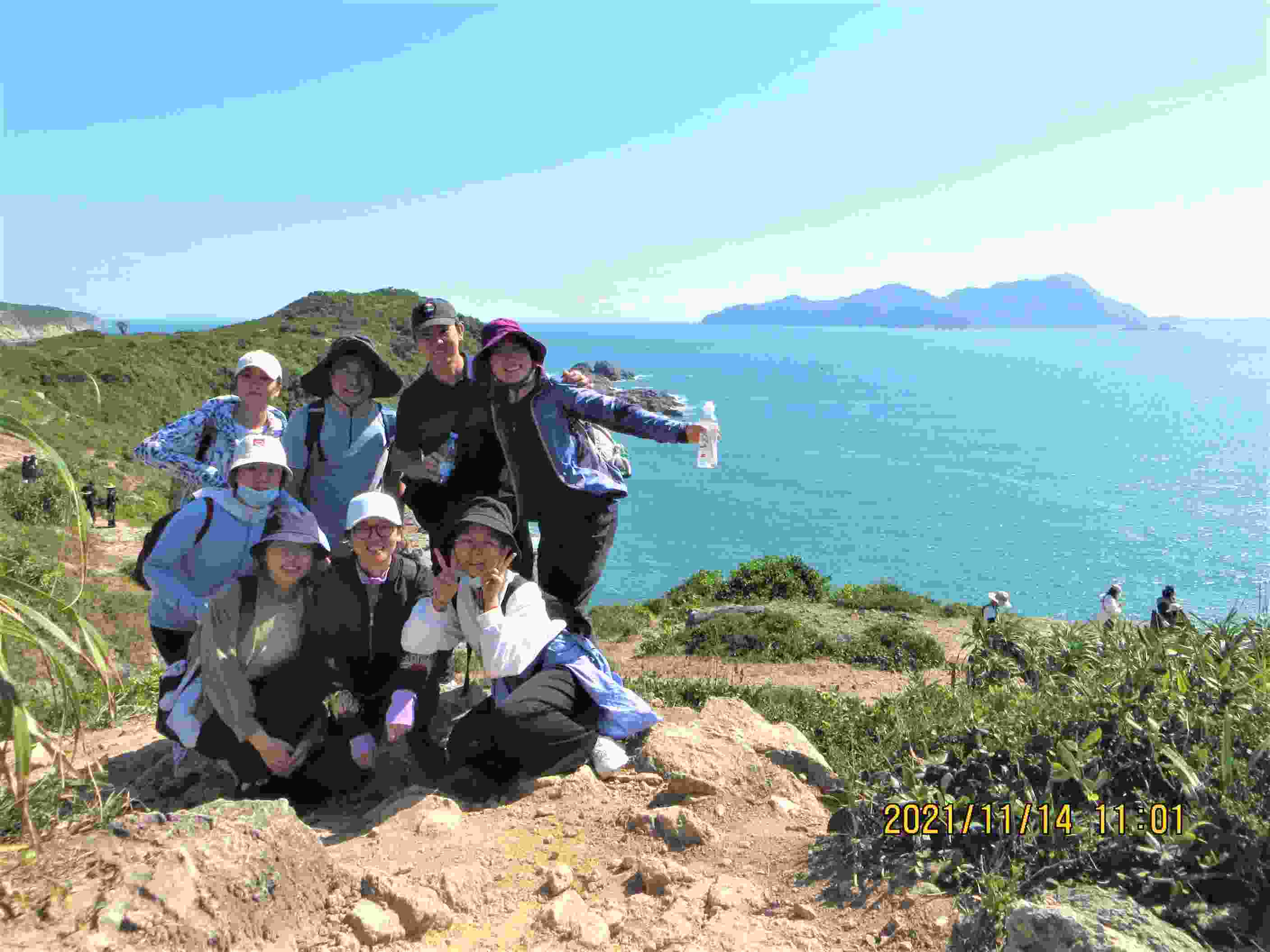 A group of eight people gather happily on an island surrounded by a beautiful sea.