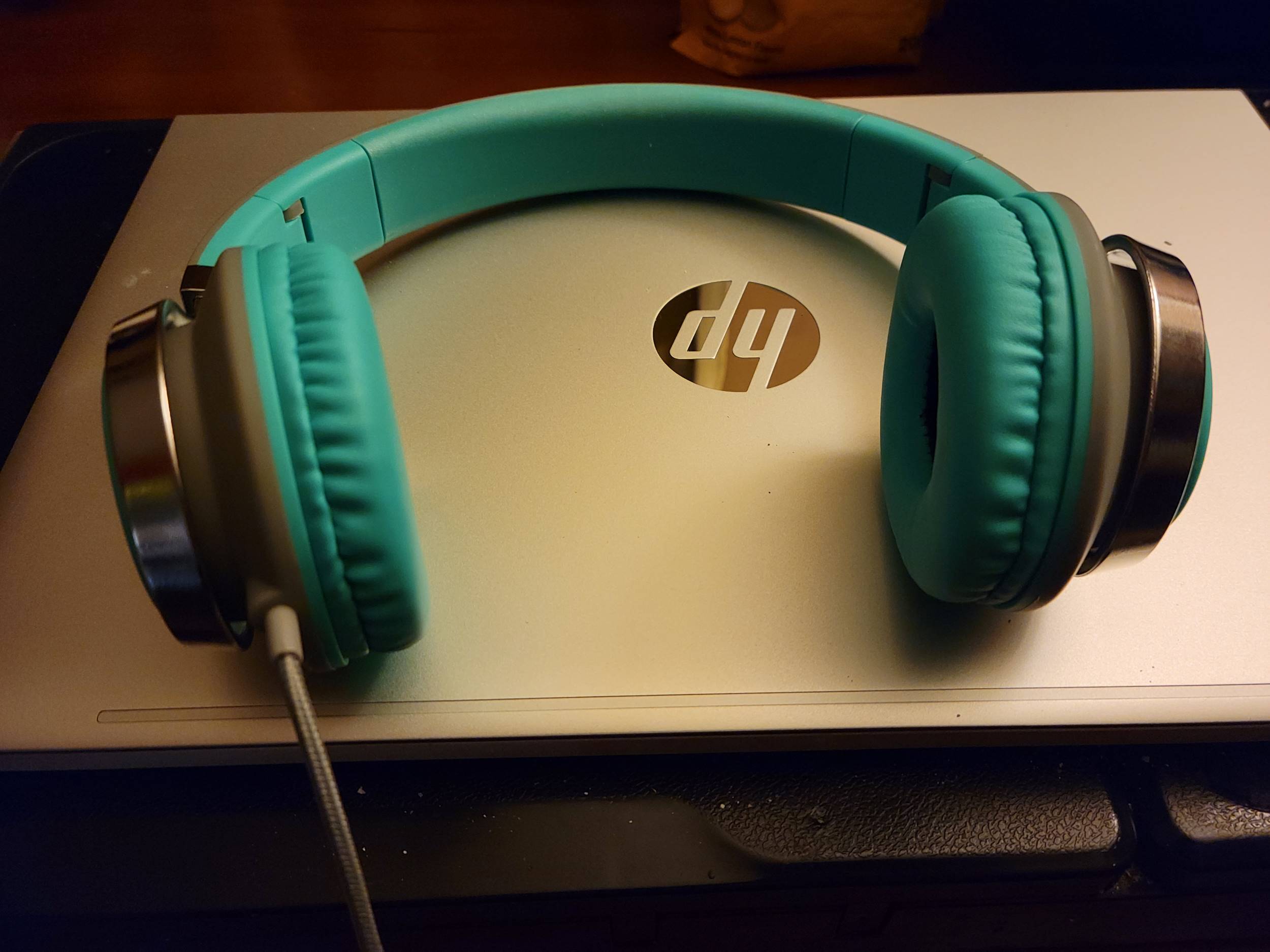 A set of teal and metallic headphones are on top of a laptop. 