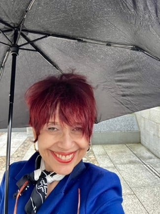 A person smiling under an umbrellaDescription automatically generated