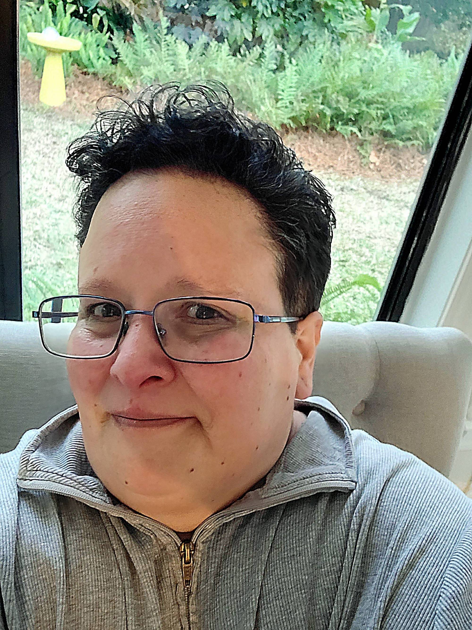 A non-binary person with short dark hair and blue metallic framed glasses looks at the camera nervously.