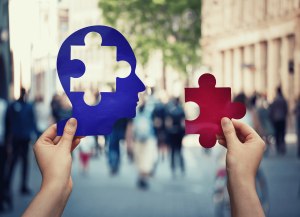 Hands holding cutouts of head and puzzle with people showing in background